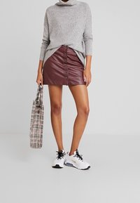 Maglione a collo alto grigio a coste, mini gonna in ecopelle borgogna con bottoni frontali e sneakers sportive bianco e nere. Borsa a tracolla a scacchi.