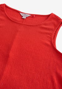 Haut de maternité rouge sans manches en tissu texturé avec encolure ronde, étiquette de marque visible à l'intérieur du col.
