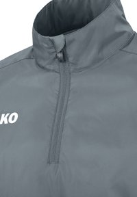 Giacca a vento grigia con zip a quarto di collo. Realizzata in un tessuto leggero e liscio, con colletto alto e dettagli del logo in bianco. Chiusura frontale con zip.