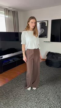 Ljusgrå bomulls-t-shirt kombinerad med löst sittande, bruna byxor med vida ben. Outfiten kompletteras med vita sneakers och visas på en texturerad grå matta.