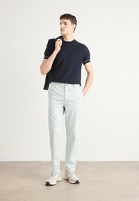 Tricou din bumbac bleumarin cu detalii albe, pantaloni mint deschis și adidași atletici gri. Modelul pozează cu un pulover bleumarin purtat pe umăr.