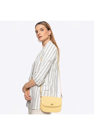 Mujer con blazer blanco y negro a rayas, mangas remangadas, llevando un bolso bandolera amarillo de cuero con herrajes dorados.