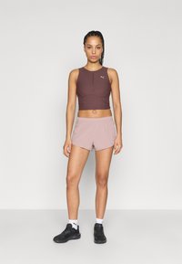 Σετ αθλητικής ένδυσης που περιλαμβάνει μπορντό crop top με φερμουάρ στο μπροστινό μέρος και ανοιχτοροζ σορτς, και τα δύο κατασκευασμένα από διαπνέον υλικό. Συμπεριλαμβάνονται μαύρα αθλητικά παπούτσια.