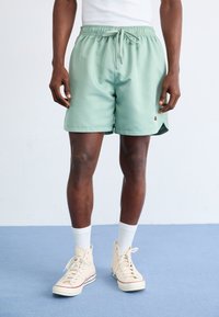 Light green swim shorts with an elastic waistband and drawstring detail. Knee-length, smooth fabric with a small logo on the side.