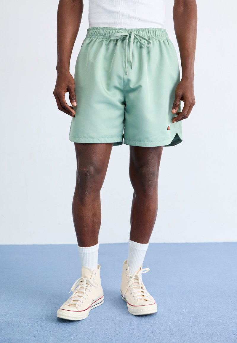 Shorts de bain vert clair avec une taille élastique et un cordon de serrage. Longueur genou, tissu lisse avec un petit logo sur le côté.