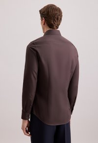 Bruine langesleevige shirt met een gladde textuur, puntige kraag en zijsplitten aan de zoom, met knoopdetails op de manchetten.