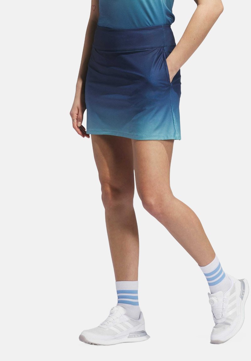 Blauwe gradient sportieve skort met textuurstof, zijzakken, een aansluitende tailleband en een sportief ontwerp. Gecombineerd met witte sneakers en gestreepte sokken.