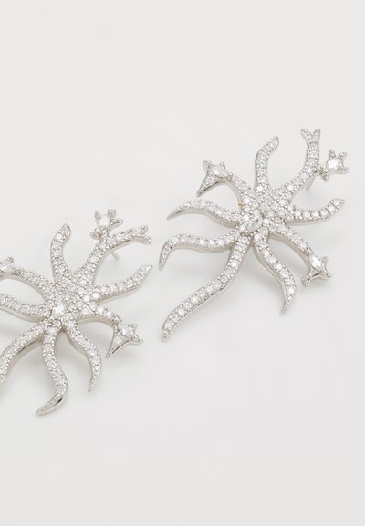 Orecchini color argento con design a stella marina, adornati con gemme trasparenti, caratterizzati da molteplici punte ondulate e dettagli intricati.