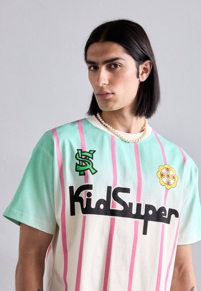 Mint green and cream t-shirt with pink vertical stripes, featuring black "KidSuper" logo and floral accents. Cotton fabric, relaxed fit.