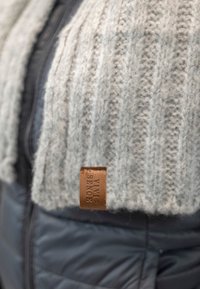 Col en pull tricoté gris avec texture côtelée, attaché à une doudoune noire ; comprend une étiquette de marque en cuir marron.