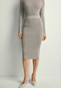 Szara, prążkowana sukienka midi z długimi rękawami i dopasowanym wcięciem w talii. Srebrne szpilki doskonale uzupełniają stylizację, podkreślając elegancki wygląd.