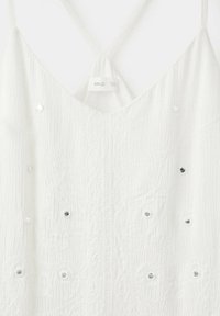 Robe blanche texturée sans manches avec fines bretelles et petits embellissements argentés dispersés, suspendue sur un fond blanc.
