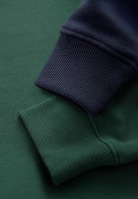 Zelene i mornarsko plave manžete na dukserici, s rebrastom teksturom, gdje je zelena manžeta ispod, a mornarsko plava manžeta složena na vrhu.