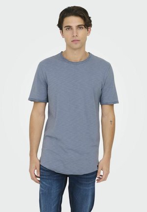 Grå kortermet t-skjorte med rund hals, med en litt lengre bakdel og en glatt tekstur. Brukt med mørk denim jeans.