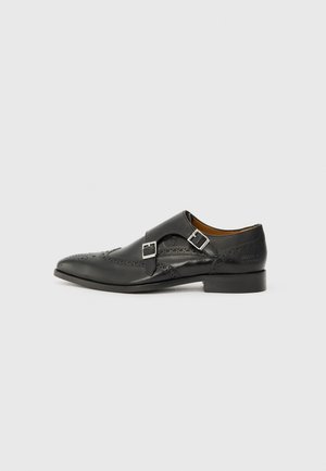 Sorte lærdressko med spiss tå, brogue-detaljer, doble sølvspenneakenter og lav hæl. Glatt overflate.