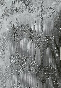 Silverfärgad tyg tätt täckt med små glänsande paljetter, vilket skapar en glittrande och reflekterande yta.