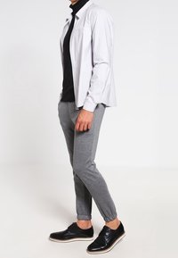 Grå joggerbyxor, åtsittande svart polotröja och en ljusgrå skjorta med knappar och en enda bröstficka. Svarta skor med vita sulor.