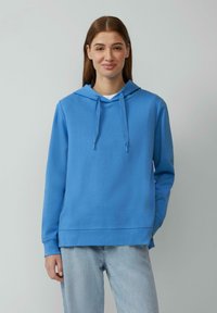 Felpa con cappuccio blu in tessuto morbido, con tasca a marsupio e stringhe. Abbinata a un paio di jeans blu chiaro, creando un look informale.