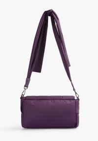 Lilla quiltet taske med en glat tekstur, kort top-hank, justerbar skulderrem og metalhardware. Rektangulær form, minimalistisk design.