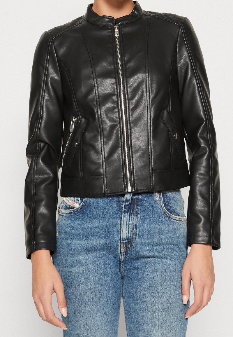 Zwarte leren cropped jack met een rits aan de voorkant, doorgestikte schouderdetails en twee schuine zijzakken, gecombineerd met lichtblauwe spijkerbroeken.