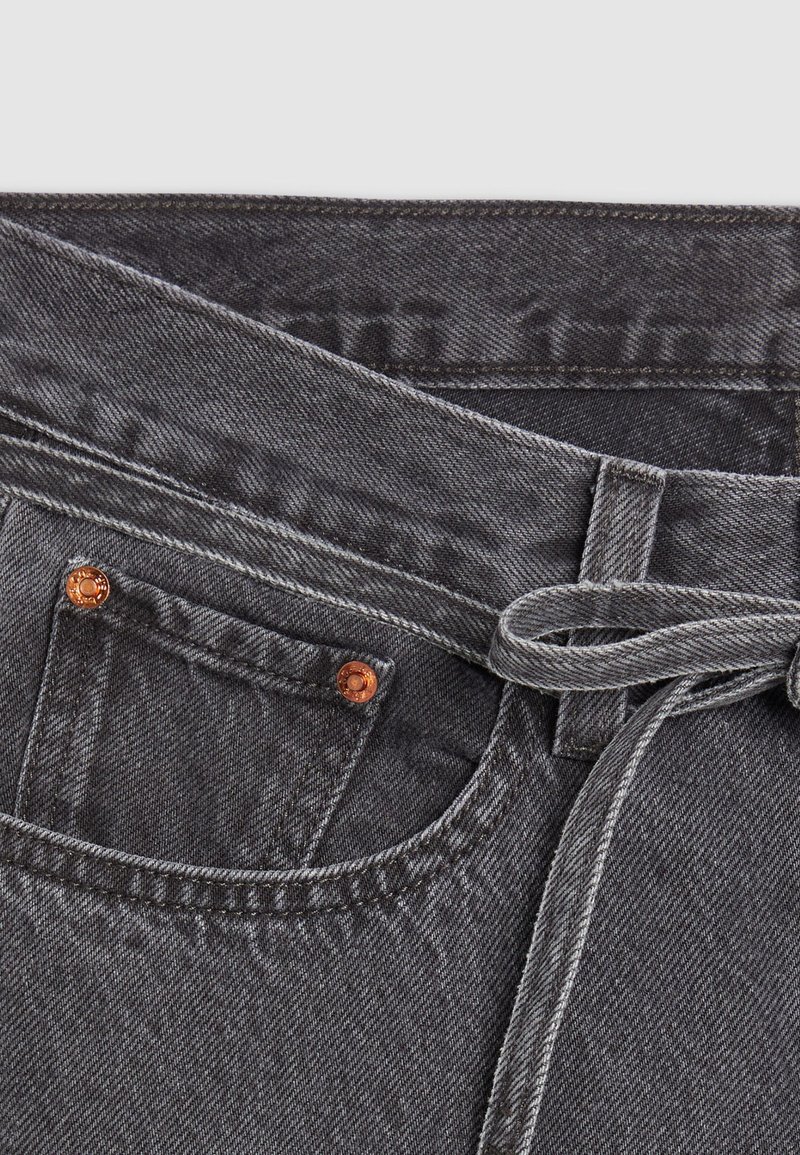 Dunkelgraue Denim-Jeans mit Bindegürtel, kupferfarbenen Nieten und subtiler Textur. Einschließlich frontaler Taschen und genähten Details.
