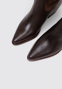 Bottines en cuir marron avec une finition texturée, bout pointu et un petit talon carré, dotées d'un intérieur lisse et d'une couture minimale.
