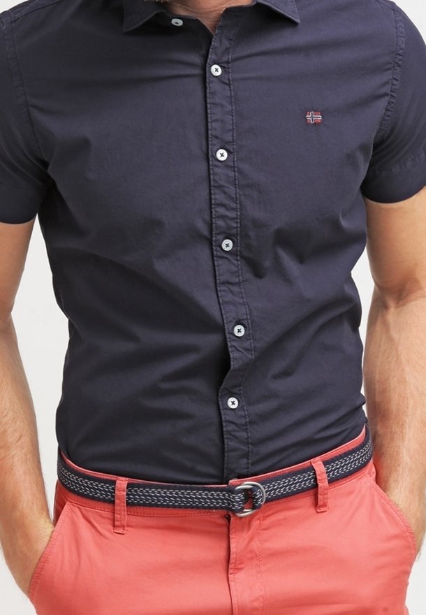 Marinblå kortärmad skjorta med knapp-down krage, med vita knappar och en liten logotyp. Kombinerad med ljus korallfärgade byxor och ett mönstrat bälte.