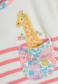 Biała bawełniana bluzka w różowe paski. Posiada teksturowaną żółtą żyrafę oraz kieszeń w kwiatowy wzór z pastelowymi kwiatami.