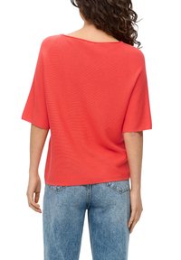 Koralfarbenes kurzärmliges Strickoberteil mit weitem Ausschnitt und lässiger Passform. Kombiniert mit hochtaillierten blauen Jeans.
