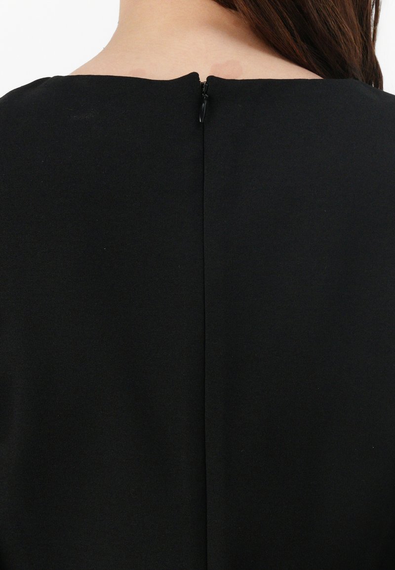 Abito nero con collo alto e chiusura con zip sul retro. Texture liscia e design semplice senza motivi o decorazioni.