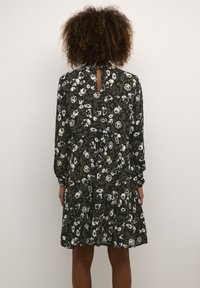 Blumenkleid in Dunkelgrün mit weißen Blumen, mit langen Ärmeln, einer Schlüsselloch-Rückseite und einem gestuften Rockdesign. Weicher Stofftextur.