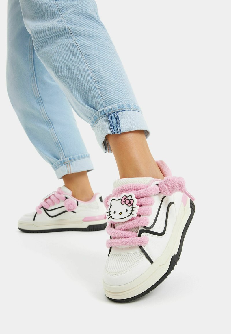 Bele teniske z roza puhastimi vezalkami in aplikacijo Hello Kitty. Črne akcentne črte na straneh, teksturiran material in gumijast podplat.