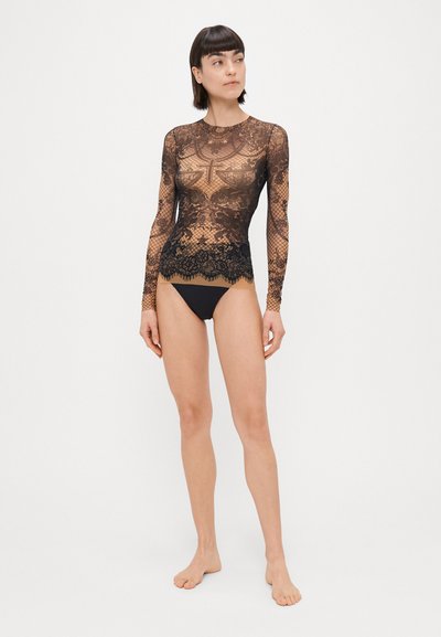 Crna čipkasta bluzica s dugim rukavima koja se ističe složenim uzorcima, uskim dizajnom i valovitom donjim rubom, u kombinaciji s jednostavnim crnim bikini donjim dijelom.