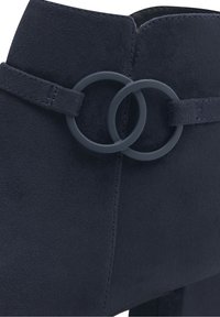 Stivale alla caviglia in suede blu navy scuro con tacco basso, caratterizzato da dettagli di fibbie circolari sovrapposte sulla fascia laterale.