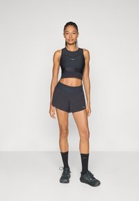 Čierny športový crop top a šortky, obe z hladkej tkaniny. Šortky majú elastický pás. Čierne ponožky a bežecké topánky dotvárajú outfit.