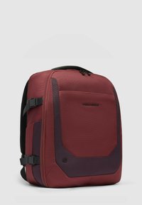 Rode rugzak met een gestructureerde afwerking, voorzien van een donker accentpaneel, verstelbare banden en een gestroomlijnd ontwerp. Ritsluiting aan de bovenkant.