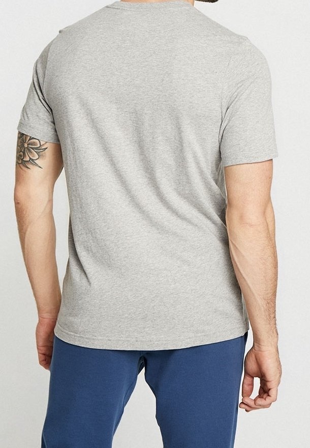 Grå bomullströja med rund hals och korta ärmar. Slät textur, figurnära design och minimal detaljering. Bärs med blå byxor.