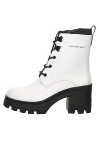Botín blanco de tobillo con cordones negros, suela gruesa negra y tacón pronunciado. Presenta un cuello acolchado y el logotipo de "Calvin Klein Jeans".
