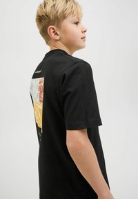Tricou negru cu mânecă scurtă, prezentând un design grafic colorat pe spate, care include secțiuni roșii, galbene, albe și albastre, împreună cu modele texturate.