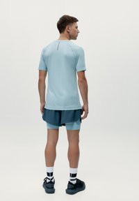 Světle modré sportovní tričko s krátkými rukávy, kombinované s tmavě modrými a světle modrými šortkami, které mají vrstvený design a texturovanou látku.