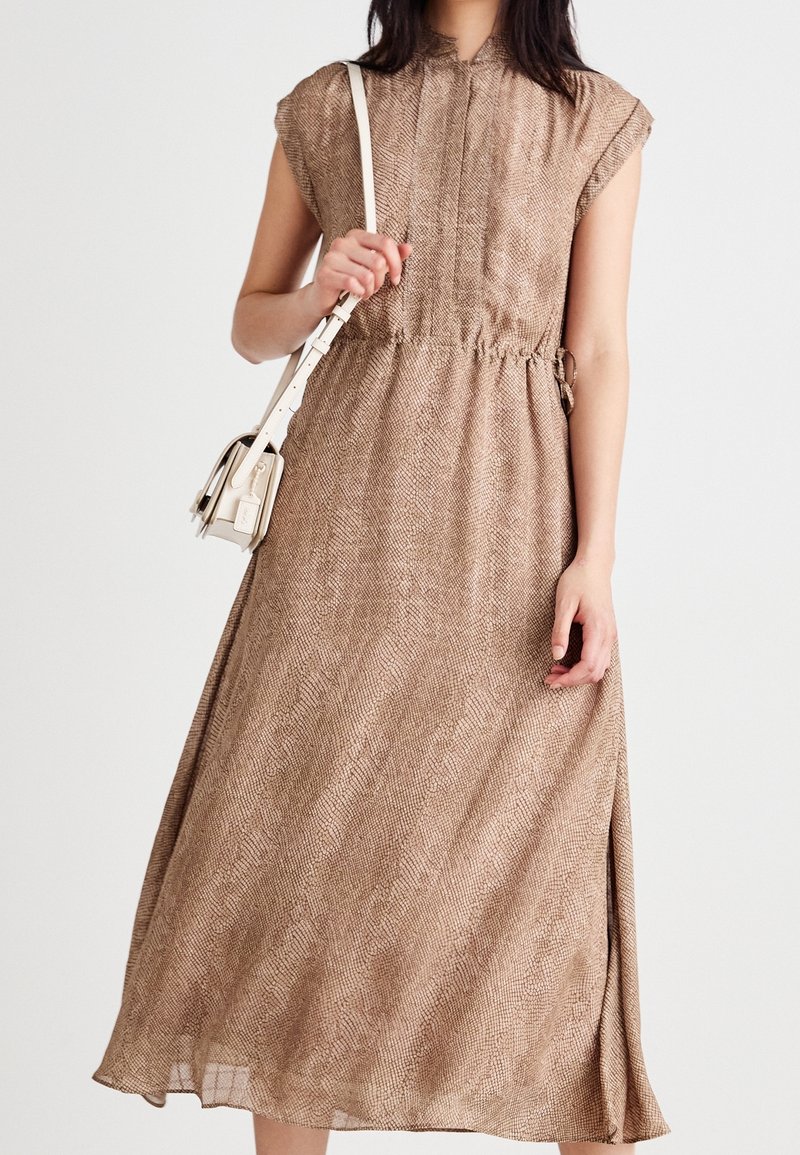 Brun vävd midiklänning med korta ärmar, samlad midja och slitsar på sidorna; tillsammans med en liten krämfärgad handväska.
