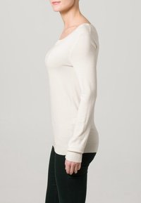 Maglione lungo con maniche a sbuffo di un beige chiaro, scollatura a barca, vestibilità aderente e polsini a costine, realizzato in morbido tessuto texturizzato.