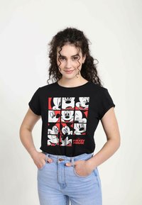 Černé tričko s grafickým designem, na kterém jsou zobrazeny různé stylizované obličeje Mickey Mouse v bílé a červené barvě, krátké rukávy a volný střih.