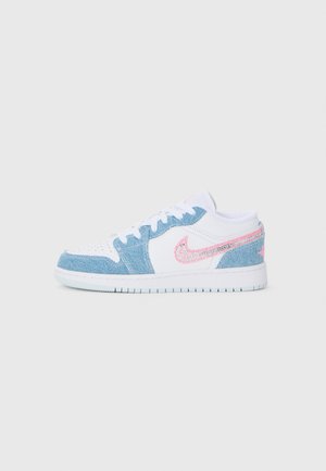 Nízke biele tenisky s ľahkým modrým denimovým prešitím a trblietavým ružovým logom Nike swoosh na boku, zobrazené na bielom pozadí.