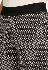 Schwarzer gemusterter Stoff mit beigen und weißen geometrischen Formen; verfügt über einen einfarbigen schwarzen elastischen Bund und ein strukturiertes Material.