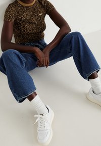 Lyhythihainen leopardikuosiset paita, siniset korkeavyötäröiset farkut, valkoiset tennarit teksturoiduilla yksityiskohdilla ja valkoiset ribbikuosiset sukat.