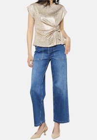 Zlatý top s leopardím potiskem s detaily v podobě zauzlování, doplněný o široké džíny s vysokým pasem v modrém denimu a tělové boty na podpatku typu mule.