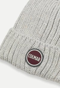 Căciulă tricotată de culoare gri deschis cu o textură răsucită. Prezintă un patch rotund burgund cu logo-ul "COLMAR" în alb.