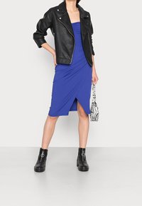 Robe bleue côtelée avec une fente sur le côté, accompagnée d'une veste en cuir noire et de grosses bottines noires à cheville. Comprend un petit sac à imprimé zèbre.