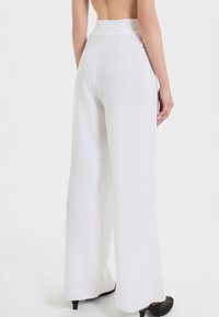 Pantaloni bianchi a gamba larga con cintura arricciata e texture liscia, caratterizzati da un design fluido che scende elegantemente fino al pavimento.